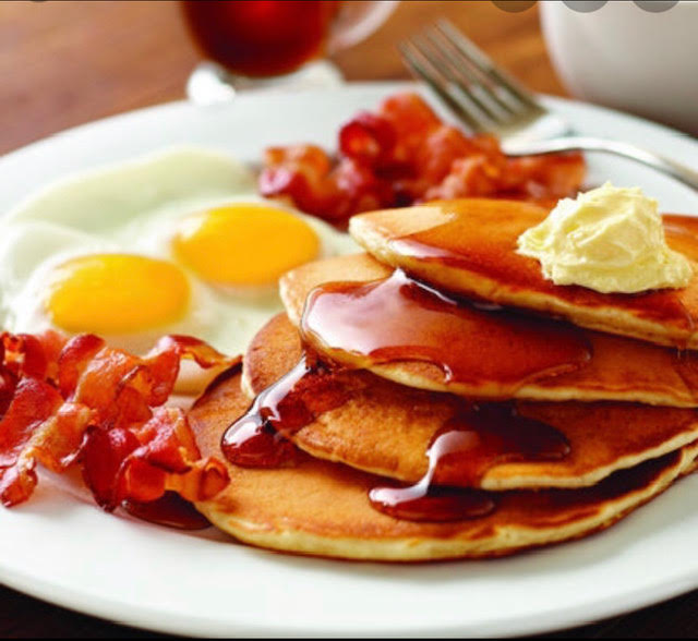 Pancakes dressed with butter and syrup, plated with bacon and eggs